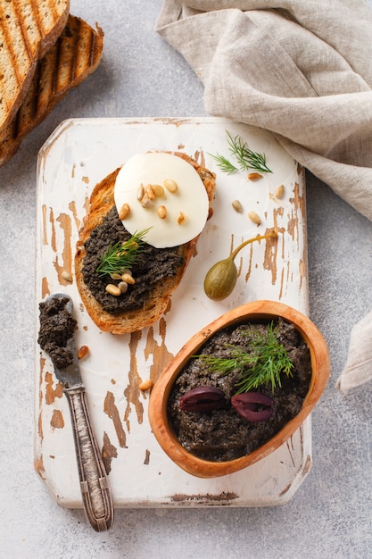 Sandwich avec tranche de mozzarella et tapenade, câpres sur fond de table rustique gris clair. Plat traditionnel provençal. Mise au point sélective