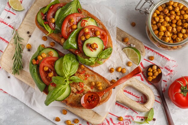 Sandwich végétarien ouvert avec tomate, concombre, pois chiches frits et basilic, vue de dessus. Concept de nourriture végétalienne saine.