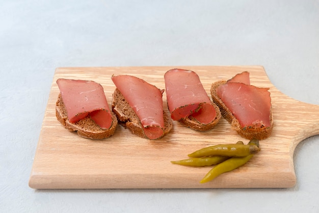 Sandwich avec de la viande séchée en tranches servie sur une planche à découper sur fond gris neutre