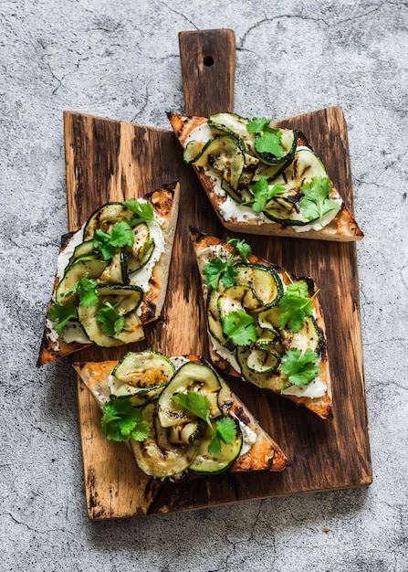 Sandwiches aux courgettes grillées et fromage à la crème sur une planche à découper sur fond gris