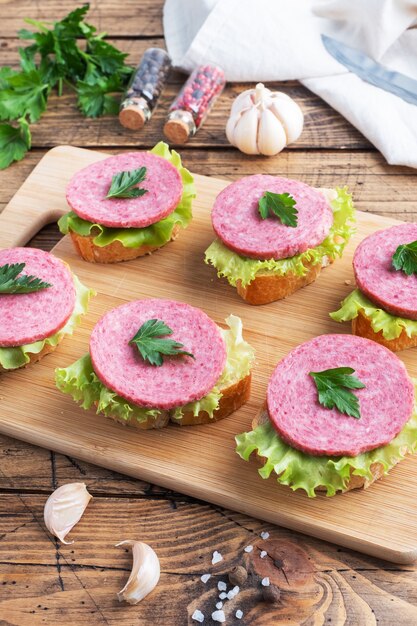 Sandwiches aux feuilles de laitue et saucisse de salami en tranches sur une planche de bois.