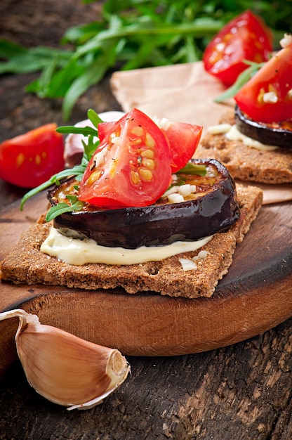 Sandwiches croustillants au régime végétarien avec fromage à la crème à l'ail, aubergines grillées, roquette et tomates cerises sur une vieille surface en bois