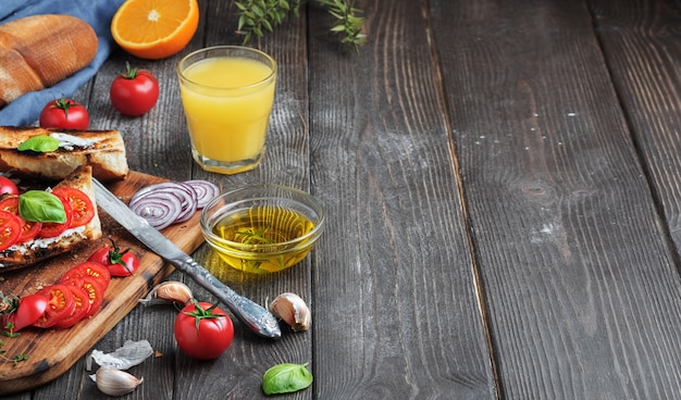 Sandwiches frais baguette, tomates, légumes et huile d'olive, ingrédients pour faire un sandwich végétalien, gros plan. Jus d'orange fraîchement pressé dans un verre Fond en bois foncé, copiez l'espace pour le texte