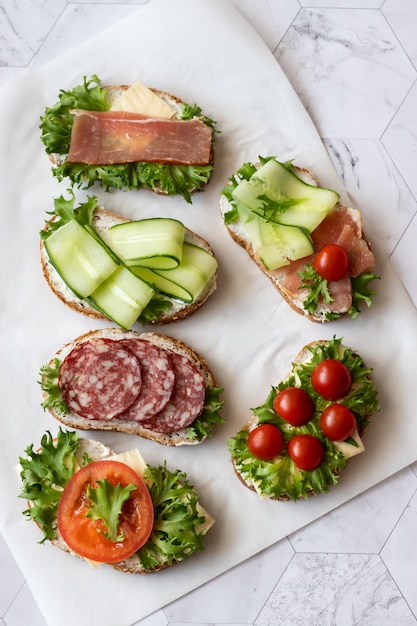 Sandwiches frais avec saucisses, fromage, bacon, tomates, laitue, concombres sur marbre
