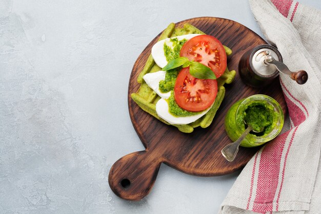 Sandwiches sur gaufrette verte avec épinards et fromage mozzarella, sauce pesto, tomates et basilic sur une vieille table en béton gris. Mise au point sélective. Vue de dessus.