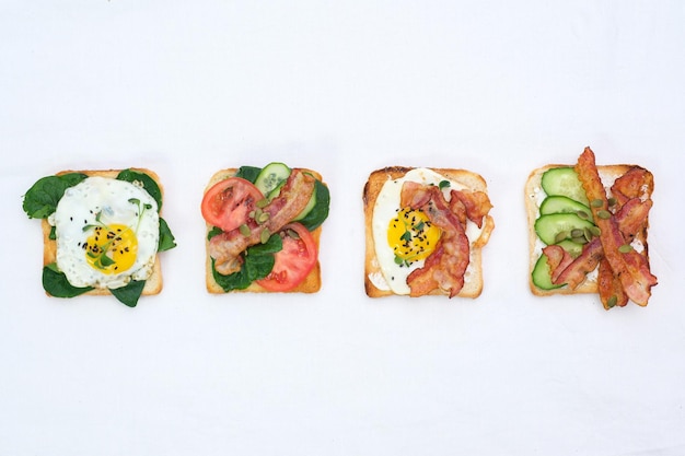 sandwiches avec des œufs frits, du jambon frit, des tomates, des concombres, du poivre sur fond blanc, vue du haut