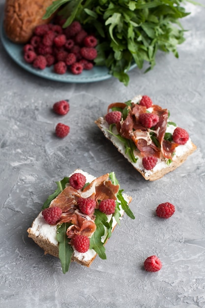 Sandwiches avec pain de grains entiers, fromage maison, roquette, jambon et framboise juteuse. Collation saine.