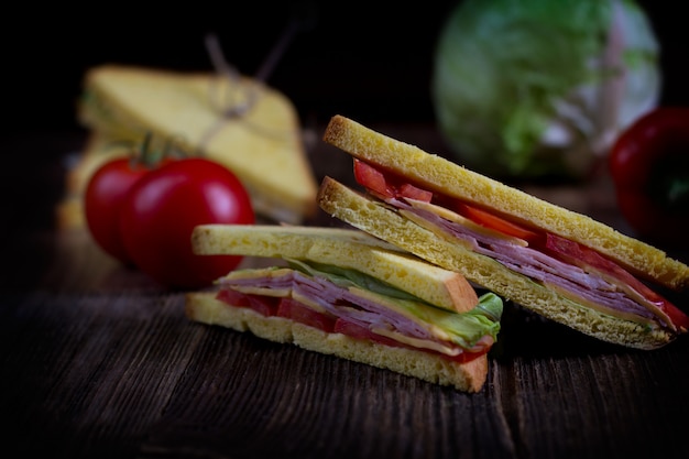 Sandwiches de pain grillé avec du fromage, jambon et légumes sur fond de bois foncé.