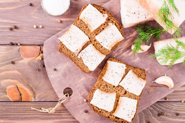 Sandwiches de pain de seigle et de bacon salé sur une planche à découper sur une table en bois.