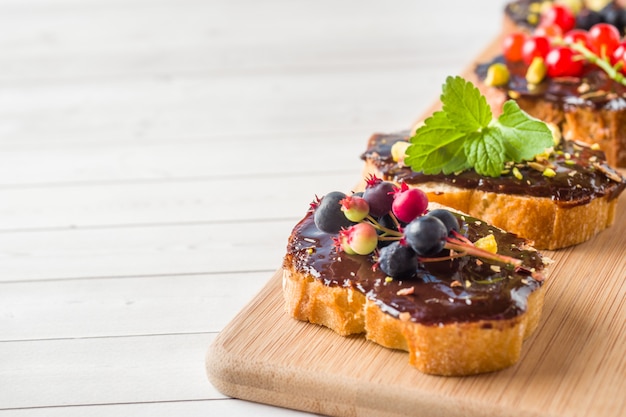 Sandwiches à la pâte de chocolat, aux pistaches et aux baies fraîches sur un plateau en bois. Espace de copie