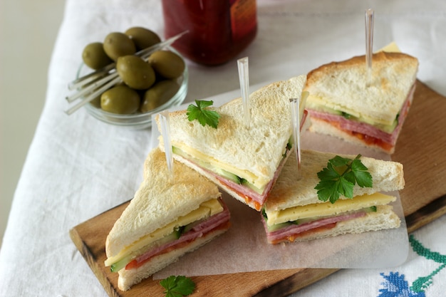 Sandwiches avec saucisse, viande, fromage et légumes frais sur une table avec des olives et du ketchup.