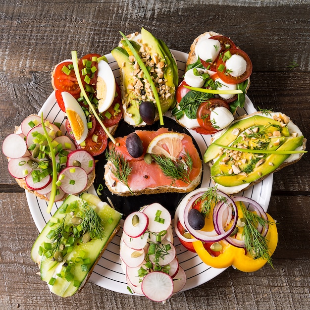 Photo sandwiches ou tapas avec du pain, du fromage à la crème, des légumes et des garnitures savoureuses.