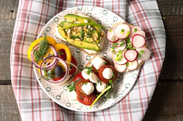 Sandwiches ou tapas avec du pain, du fromage à la crème, des légumes et des garnitures savoureuses.