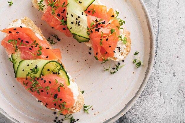 Sandwiches Toast au saumon avec fromage à la crème concombre sésame noir et micro-verts sur fond de table en béton gris Fruits de mer Alimentation saine Vue de dessus