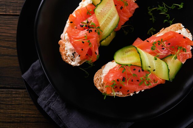 Sandwiches Toast au saumon avec fromage à la crème concombre sésame noir et micro-verts sur fond de table en bois ancien Fruits de mer Aliments sains Photographie en mode discret Vue de dessus