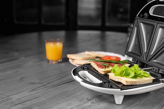Sandwichs appétissants au jambon et aux herbes dans une machine à sandwich sur fond noir et blanc