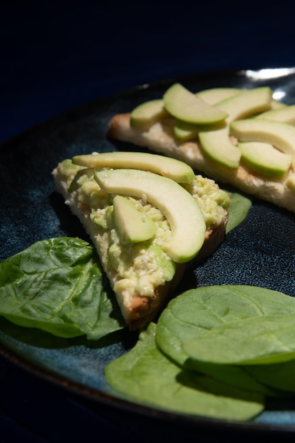 Sandwichs sur une assiette avec avocat et épinards sur fond sombre