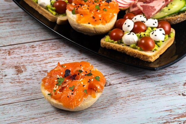 Sandwichs assortis avec du poisson, du fromage, de la viande et des légumes sur une plaque noire