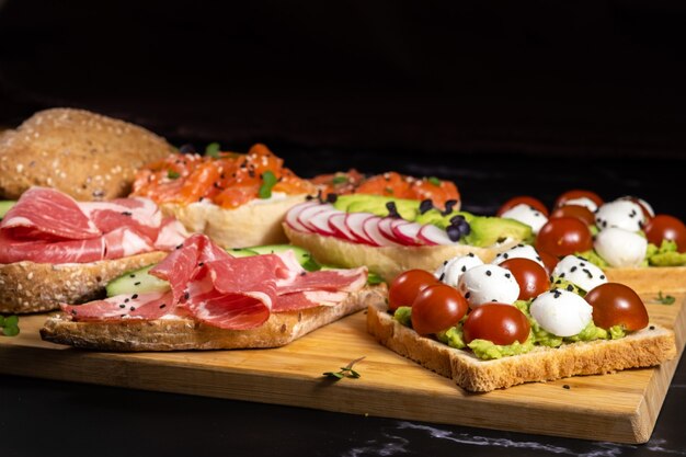Sandwichs assortis avec du poisson, du fromage, de la viande et des légumes se trouvant sur la planche