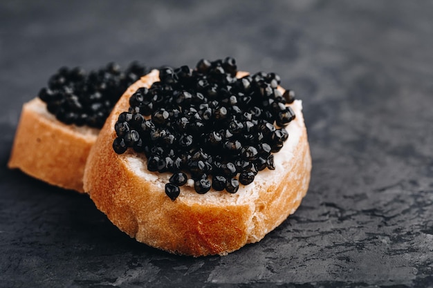 Sandwichs au caviar noir avec du beurre sur fond de béton foncé