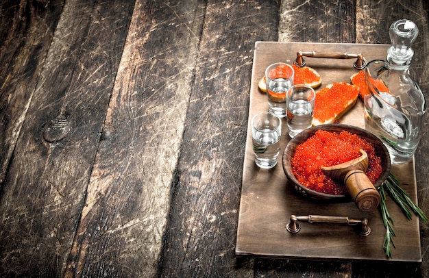 Sandwichs au caviar rouge et vodka sur un plateau. Sur fond de bois.