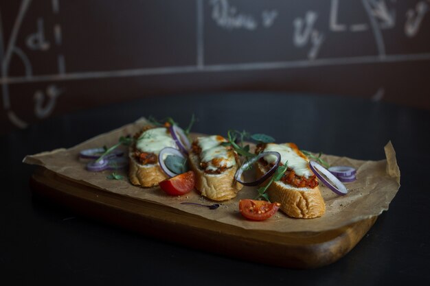 Sandwichs au pain blanc avec pâté de viande avec rondelles d'oignon rouge avec roquette et tranches de tomates fraîches rouges sur une planche de bois dans un restaurant. Nourriture délicieuse et dîner sain