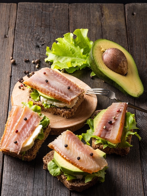 Sandwichs au poisson fumé et avocat sur une planche sur fond sombre