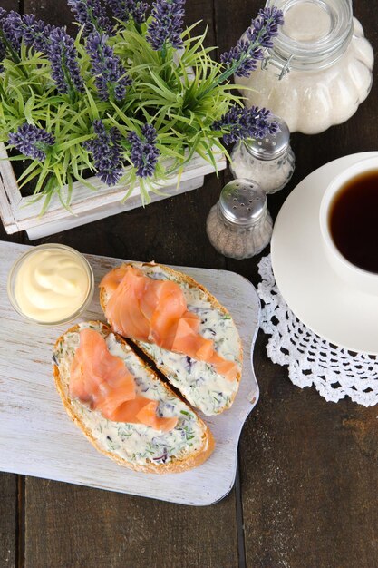 Sandwichs au poisson et tasse de thé sur une planche à découper sur une table en bois