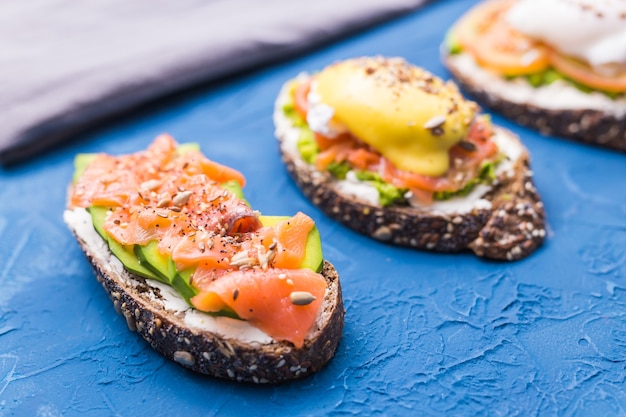 Sandwichs au saumon fumé, œufs, sauce et avocat sur fond bleu. Concept de petit-déjeuner et