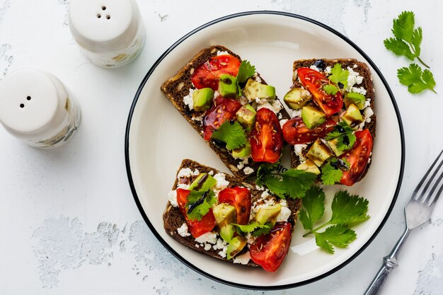 Sandwichs aux avocats, tomates cerises et fromage feta avec sauce balsamique et coriandre. Vue de dessus.