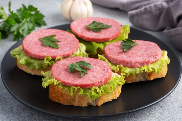 Sandwichs aux feuilles de laitue et saucisse de salami en tranches sur plaque noire.