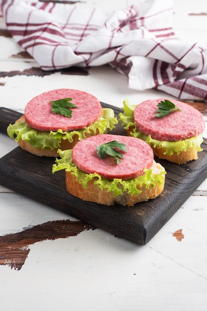 Sandwichs aux feuilles de laitue et saucisses de salami tranchées sur une planche en bois. Espace de copie