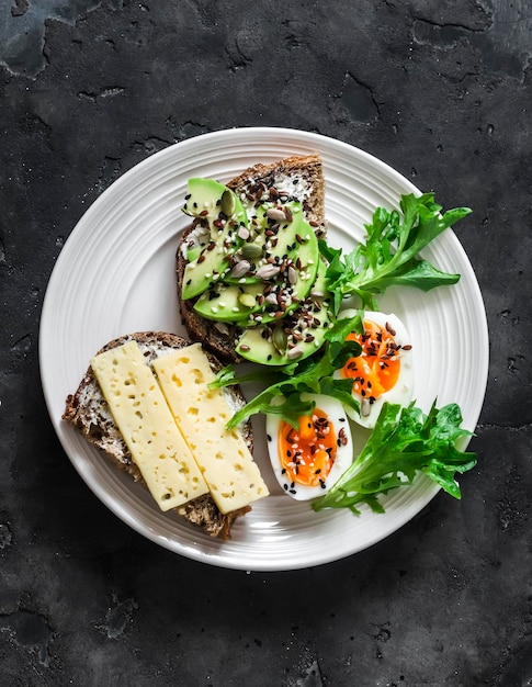 Sandwichs aux graines de fromage à l'avocat et œuf à la coque délicieux petit déjeuner collation sur fond sombre vue de dessus