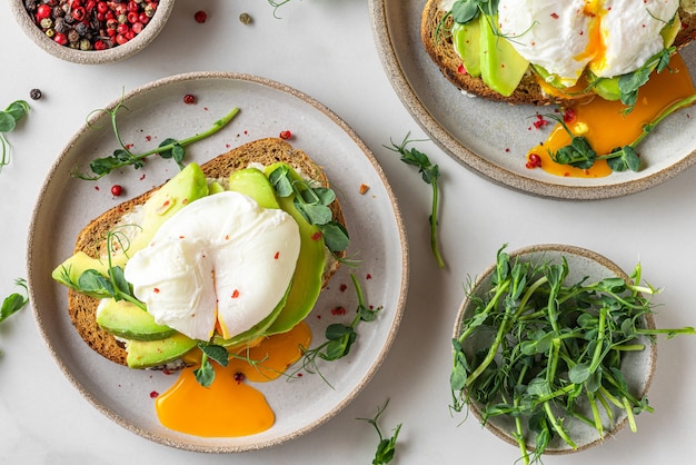 Sandwichs à l'avocat, œuf poché, pousses et fromage pour un petit-déjeuner sain sur blanc