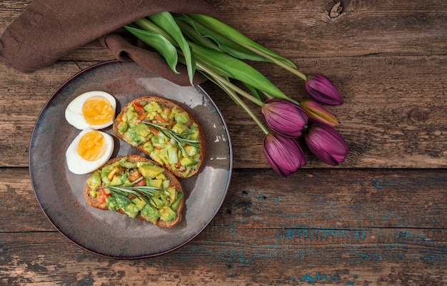 Sandwichs à l'avocat, œufs et tulipes sur un fond en bois. Le concept d'arrière-plans culinaires festifs.