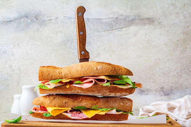 Sandwichs baguette avec viande, fromage et légumes sur planche de bois.