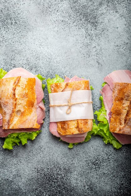 Sandwichs ciabatta frais avec jambon, fromage, laitue sur fond de béton pierre, gros plan, vue de dessus. Faire des sandwichs sains pour un concept de collation ou de déjeuner