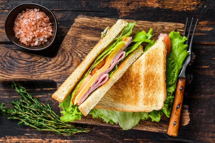 Photo sandwichs club jambon de dinde avec fromage, tomates et laitue sur une planche à découper en bois. fond en bois foncé. vue de dessus.