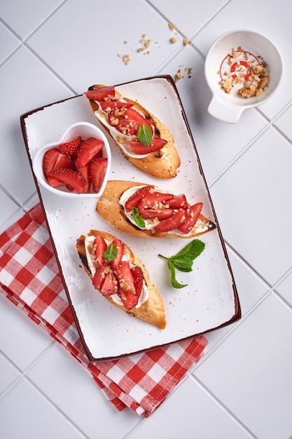 Sandwichs ouverts avec fraises, fromage à pâte molle, menthe et noix dans une assiette en céramique sur fond de pierre gris clair. Aliments diététiques d'été et sains, concept de nourriture végétarienne. Vue de dessus.