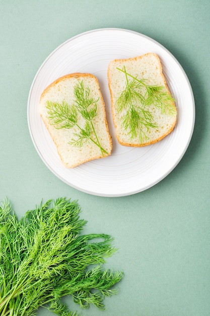 Sandwichs de pain blanc et d'aneth frais sur une assiette et un bouquet d'aneth sur fond vert. Les herbes vitaminées dans une alimentation saine. Vue de dessus et verticale