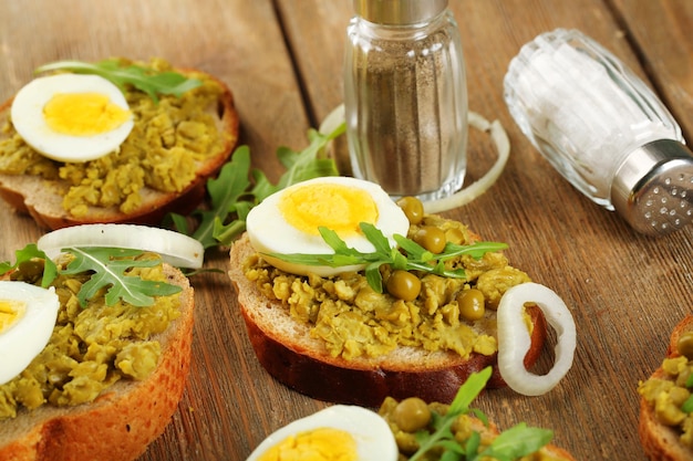 Sandwichs à la pâte de pois verts et œuf à la coque avec rondelles d'oignon et citron sur fond de planches de bois