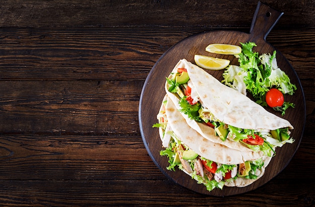 Sandwichs pita avec viande de poulet grillée, avocat, tomate, concombre et laitue servis sur bois