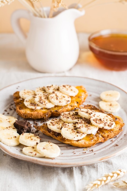 Des sandwichs prêts à manger avec de la banane au miel et du chocolat sur une assiette et un bol avec du miel sur la table En-cas végétarien fait maison