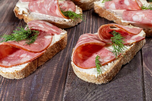 Sandwichs à la saucisse fumée et au fromage à la crème. Décoré avec des herbes à l'aneth. Sur un fond en bois sombre. Copiez l'espace.