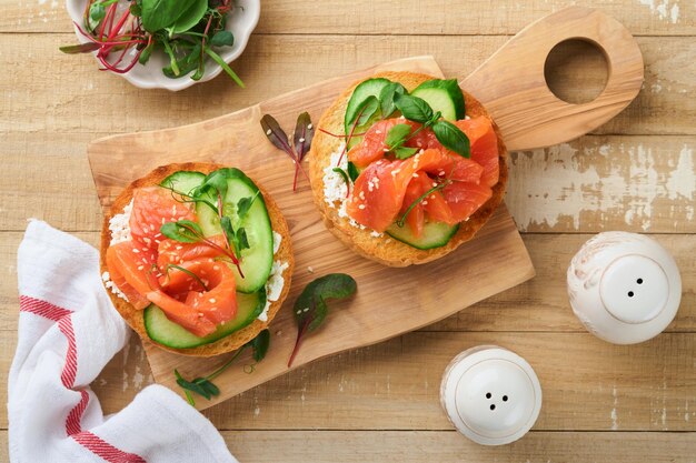 Sandwichs de saumon fumé ouverts avec fromage à la crème concombre graines de sésame microgreens épinards et feuilles de pois sur un fond en bois vieux léger petit déjeuner sain collation délicieuse vue supérieure