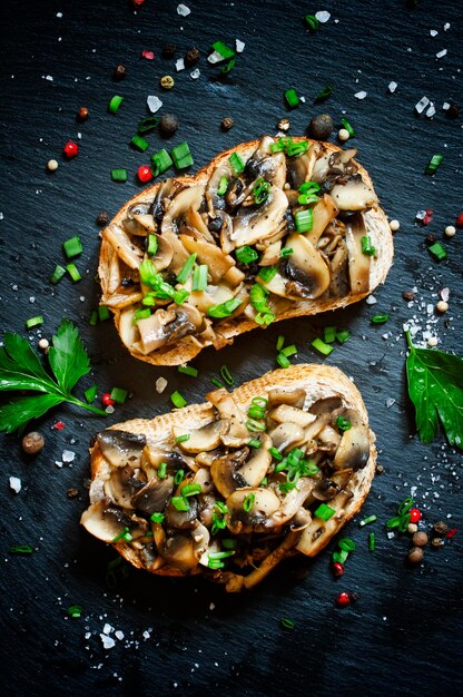 Sandwichs savoureux aux champignons grillés et oignons verts avec du pain de son sur fond sombre vue de dessus