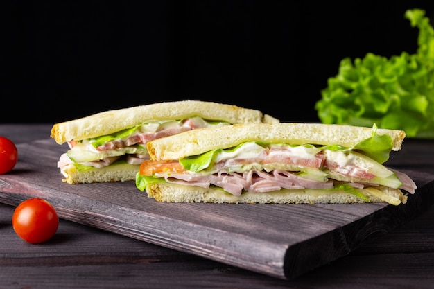 Sandwichs triangulaires avec pain grillé, laitue et légumes sur fond sombre. Petit-déjeuner ou déjeuner sain et délicieux.