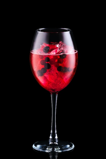 Sangria froide avec des baies de forêt dans un verre à vin isolé sur fond noir