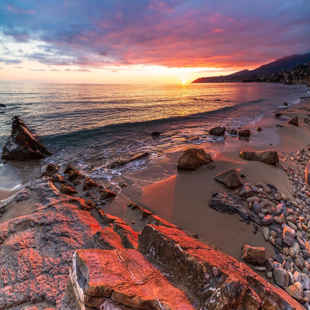 Sanremo, Riviera dei Fiori, Ligurie, Italie. Scenis rochers et galets sur la plage illuminés par la lumière du coucher du soleil. Ciel coloré dramatique agitant la mer.