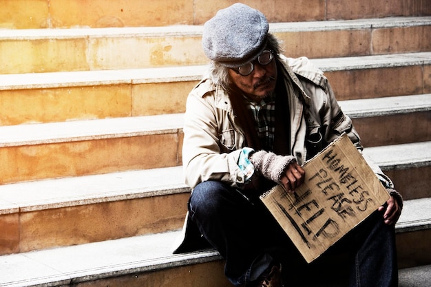 Photo un sans-abri tenant un panneau alors qu'il est assis sur les marches